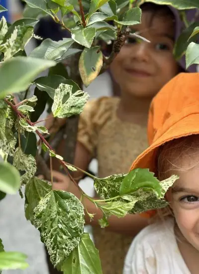 Two children peeking through native garden leaves at Natural Elements Early Learning Merrimac